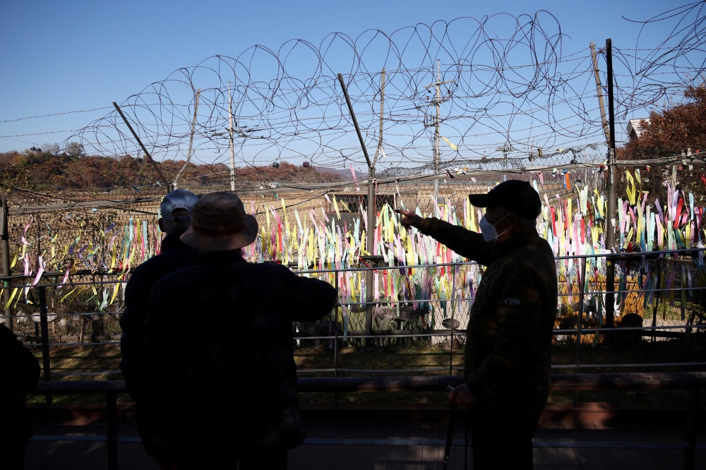 FILE PHOTO: Men look at a military fence decorated with ribbons bearing messages wishing for the reunification of the two Koreas near the demilitarized zone separating the two Koreas, in Paju, South Korea, November 4, 2022. REUTERS/Kim Hong-Ji