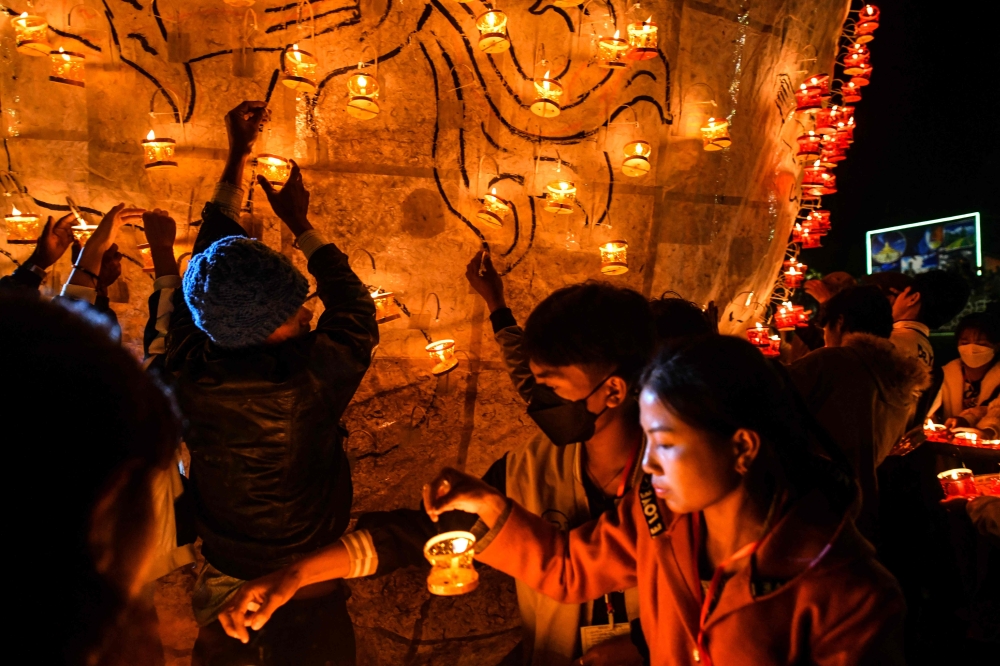 This photo taken on November 6, 2022 shows revellers preparing lanterns to attach to hot-air balloons during the Tazaungdaing Lighting Festival at Pyin Oo Lwin Township in Mandalay. (Photo by AFP)