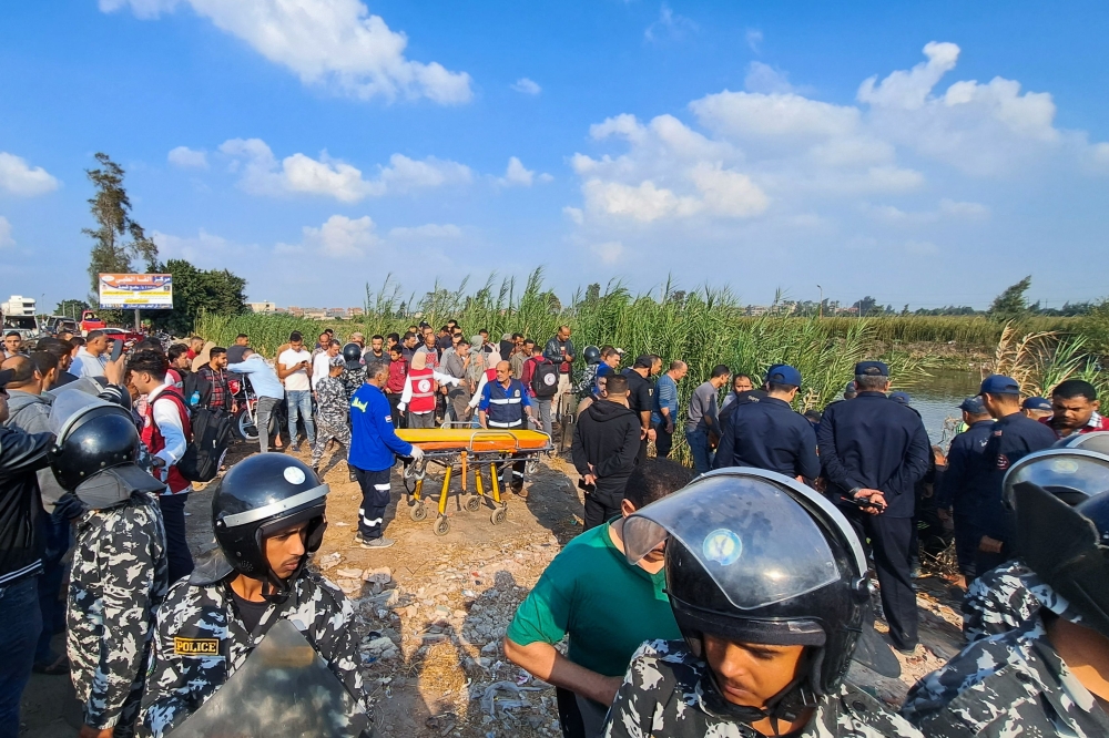 People gather near Egyptian emergency service personnel during the search for survivors after a minibus fell into a canal in al-Dayris village near the Nile Delta city of Mansoura in the Dakahlia Governorate, some 120Km north of the capital, on November 12, 2022. (Photo by Khaled DESOUKI / AFP)