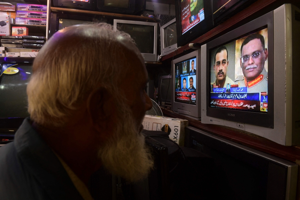 A man watches a news television broadcast of the nomination of the next Pakistan's army Chief General Syed Asim Munir (on television 2R), at a market in Karachi on November 24, 2022. (AFP/Asif Hassan)