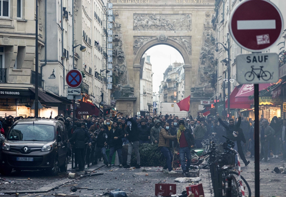 Protestors stand in front of riot police officers following a statement by French Interior Minister Gerald Darmanin (unseen) at the site where several shots were fired along rue d'Enghien in the 10th arrondissement, in Paris on December 23, 2022. (Photo by Thomas Samson / AFP)