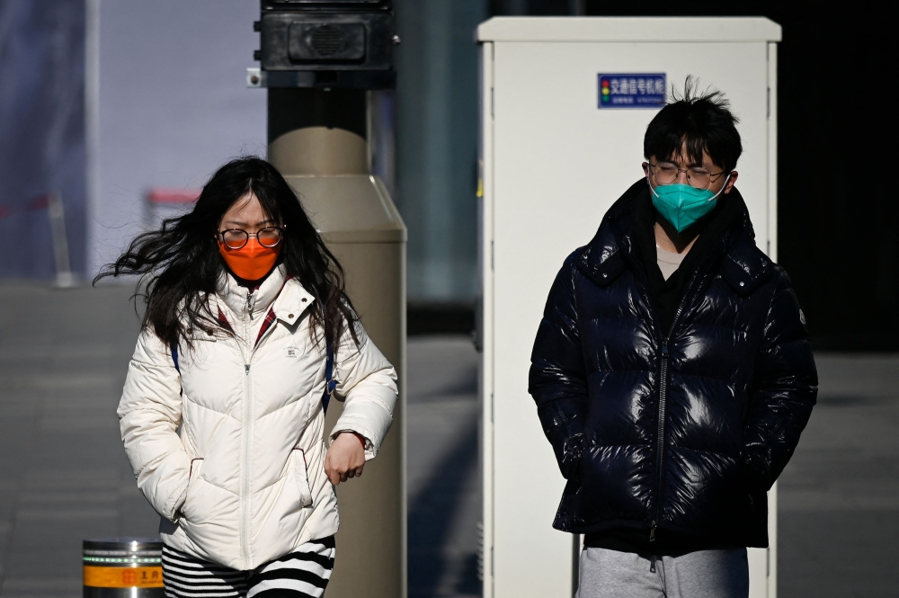 People cross a street in Beijing on December 26, 2022. (Photo by Wang Zhao / AFP)