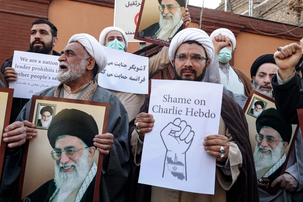 Demonstrators gather with images of Iran's supreme leader Ayatollah Ali Khamenei during a protest against defamatory cartoons depicting him published by French satirical weekly Charlie Hebdo, outside the French embassy in Iran's capital Tehran on January 8, 2023. (Photo by ATTA KENARE / AFP)