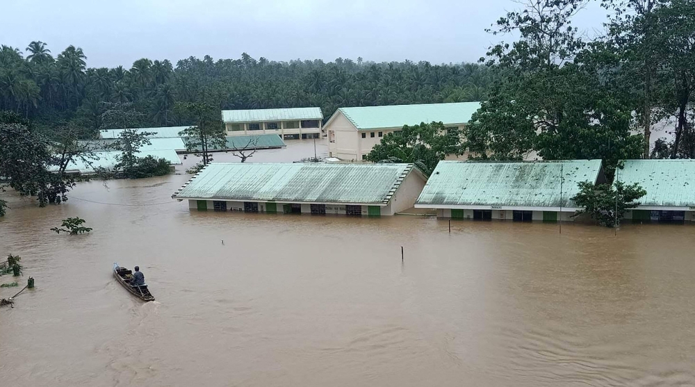 This handout photo taken and released on January 10, 2023 from Jipapad Public Information Office shows a resident riding on a wooden boat as he paddles past submerged school buildings, due to floodings brought about by heavy rains in Jipapad town, Eastern Samar province, South of Manila. (Photo by Handout / Jipapad Public Information Office / AFP)