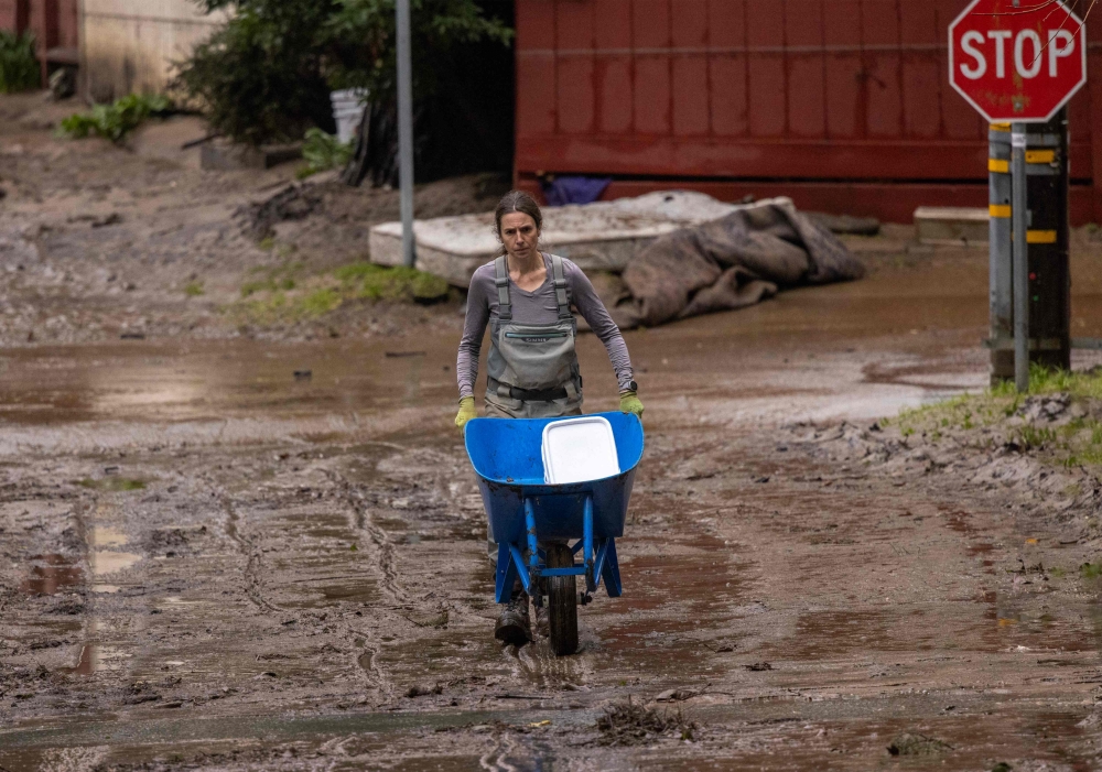 A resident cleans up mud in the street in Felton, California, on August 14, 2022, as a series of atmospheric river storms continue to cause widespread destruction across the state. (Photo by DAVID MCNEW / AFP)