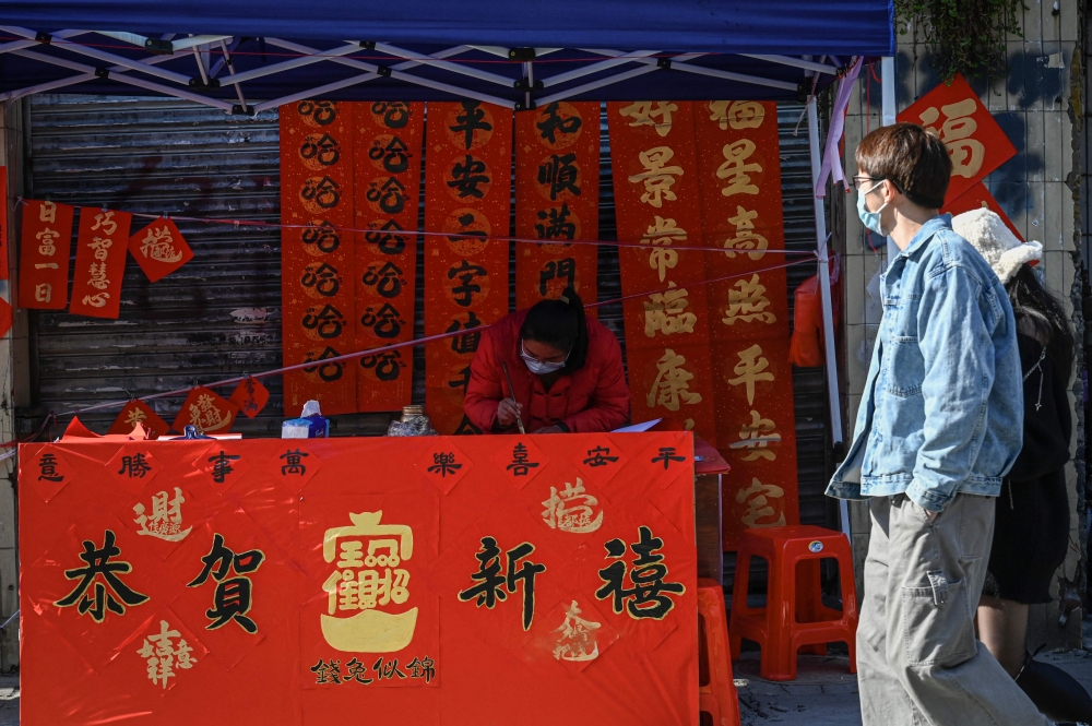 A calligrapher writes spring couplets, a kind of Lunar New Year decorations, at a stall along a street in Foshan, in southern China's Guangdong province on January 18, ahead of the start of the Lunar New Year, which ushers in the Year of the Rabbit on January 22. (Photo by Jade Gao / AFP)