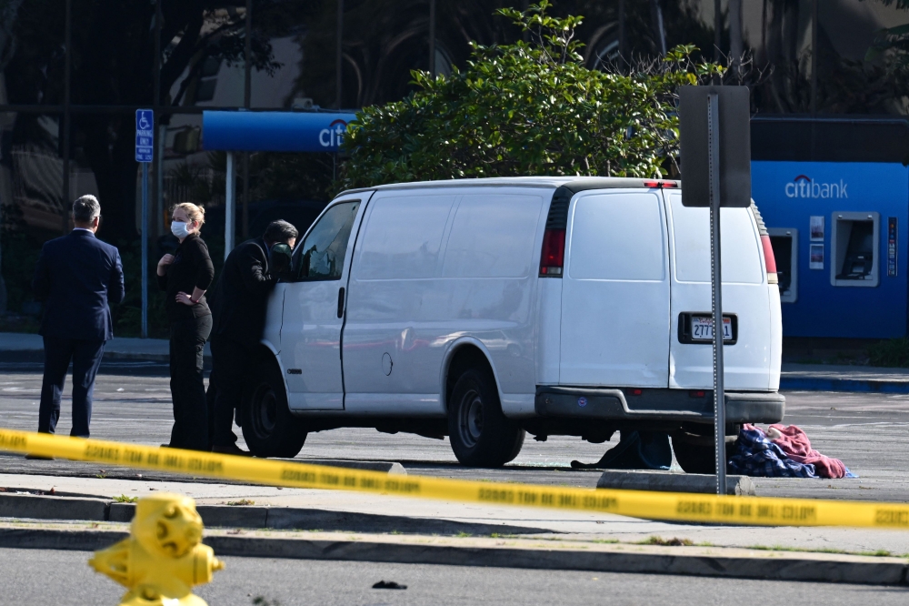 A law enforcement official looks into the window of a van with a body in the driver's seat in Torrance, California, on January 22, 2023. (Photo by Robyn Beck / AFP)