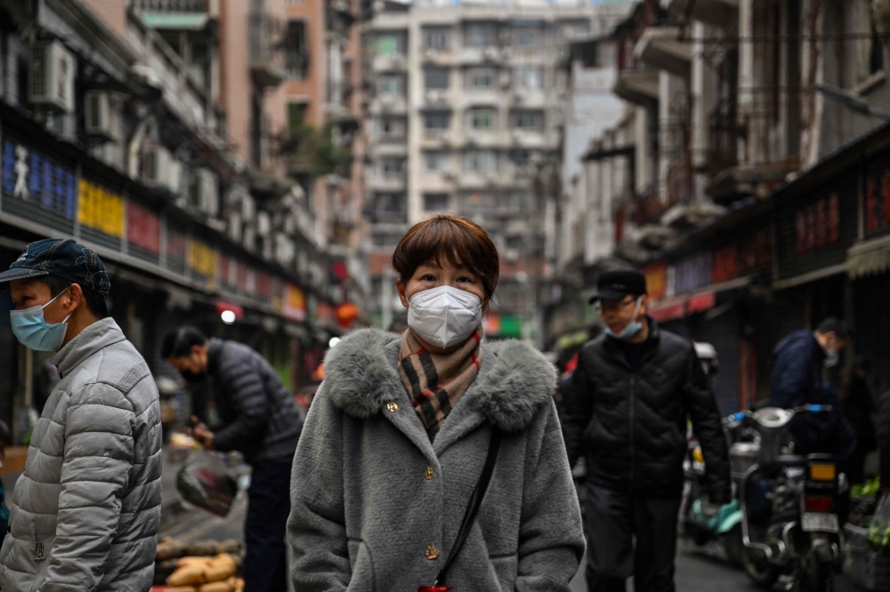 People walk down a street next to a local market in Wuhan, in China's central Hubei province, on January 23, 2023. (Photo by Hector RETAMAL / AFP)