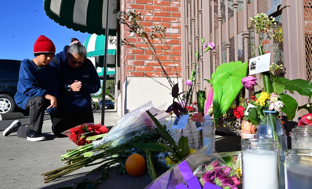 Inez Arakaki and her son Zachary offer prayers after bringing flowers to a makeshift memorial site in front of the Star Dance Studio in Monterey Park, California, on January 23, 2023, where 10 people were shot dead late on January 21, 2023. (Photo by Frederic J. Brown / AFP)