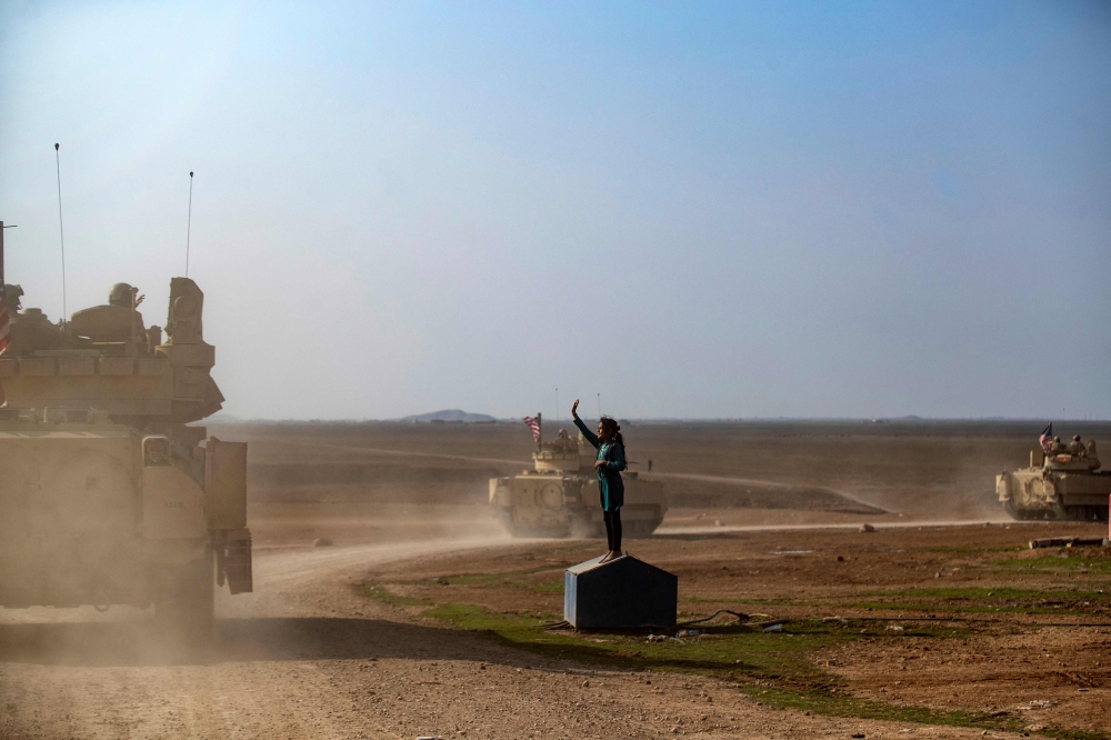 A child waves as a US convoy patrols the area near the town of Tal Hamis, southeast of the city of Qameshli in Syria's northeastern Hasakeh governorate, on January 26, 2023. (Photo by Delil Souleiman / AFP)