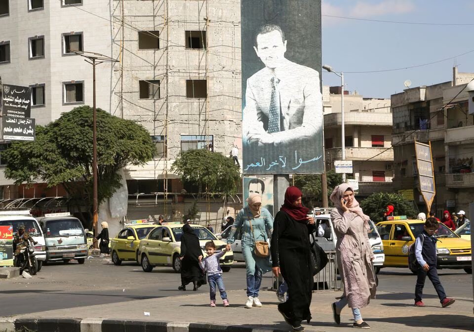 People walk near a poster depicting Syria's President Bashar al-Assad in Homs, Syria, on October 3, 2021. Picture taken October 3, 2021. File photo / Reuters