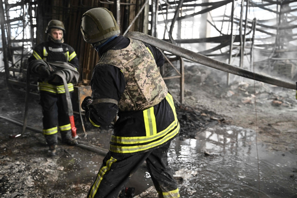 Ukrainian firefighters roll a fire hose as they work to put out fire in a shopping mall following a Russian shelling in Kherson, on February 3, 2023, amid the Russian invasion of Ukraine. (Photo by Genya SAVILOV / AFP)