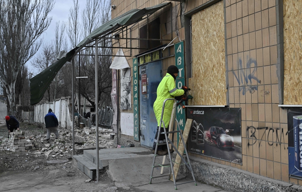People clear debris and cover broken windows in shops damaged following strike in Kherson on February 4, 2023, amid Russian invasion of Ukraine. - Russian forces have been shelling the southern region of Kherson, after withdrawing its forces from the region's main city last year. (Photo by Genya SAVILOV / AFP)