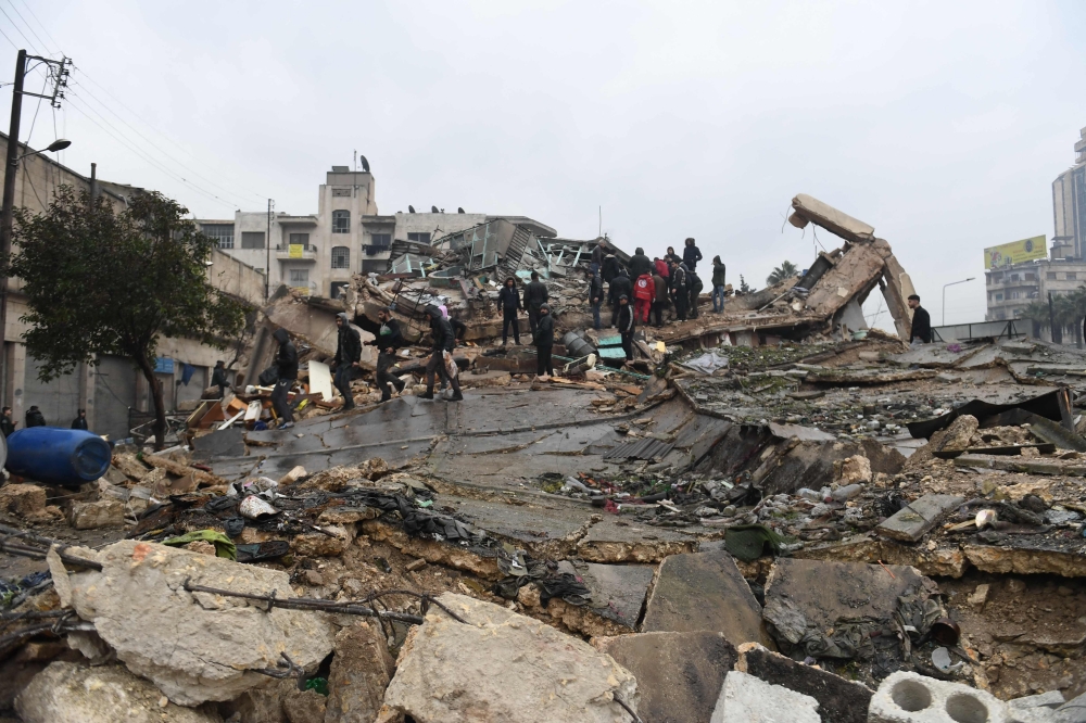 People gather around collapsed buildings as rescue teams look for survivors following an earthquake in the Syrian city of Aleppo on February 6, 2023. (Photo by AFP)