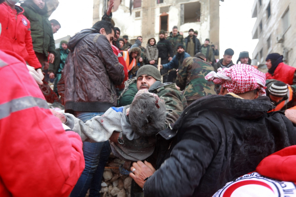 Syrian rescue teams carry a casualty picked up from the rubble after an earthquake in the government-controlled central Syrian city of Hama on February 6, 2023. - A 7.8-magnitude earthquake hit Turkey and Syria early on February 6, killing hundreds of people as they slept, levelling buildings and sending tremors that were felt as far away as the island of Cyprus, Egypt and Iraq. (Photo by LOUAI BESHARA / AFP)