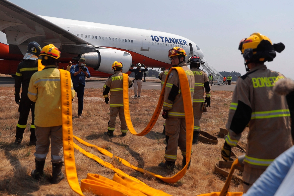 Firefighters prepare to load water into the US DC-10 Air Tanker at the Carriel Sur airport in Concepcion, Chile on February 6, 2023. - The forest fires that hit the south-central zone of Chile have already left 26 dead and have destroyed more than 1,100 homes, at a time when international aid begins to arrive to fight the flames.  (Photo by JAVIER TORRES / AFP)
 