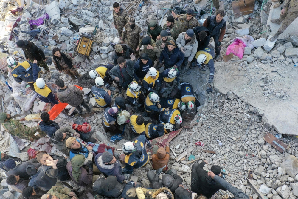 An aerial picture shows rescuers searching the rubble of buildings for casualties and survivors in the village of Besnaya in Syria's rebel-held northwestern Idlib province at the border with Turkey following an earthquake, on February 7, 2023. (Photo by Omar Haj Kadour / AFP)