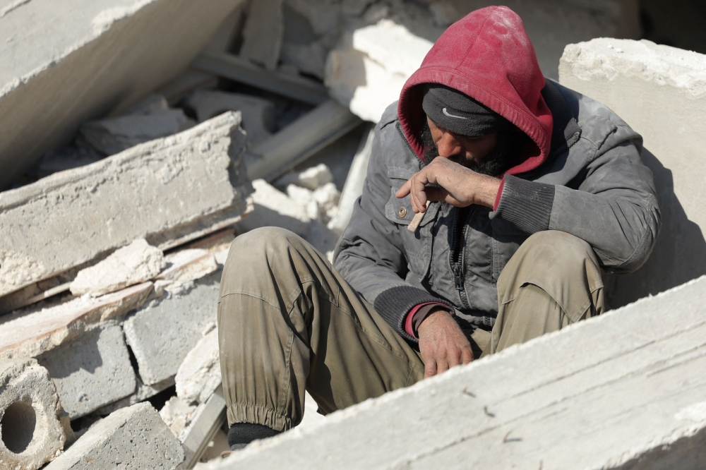 A Syrian man sits amidst the rubble as he waits for new about family members stuck under the wreckage in the town of Harim in Syria's rebel-held northwestern Idlib province on the border with Turkey, on February 8, 2023, two days after a deadly earthquake that hit Turkey and Syria. (Photo by Omar HAJ KADOUR / AFP)
