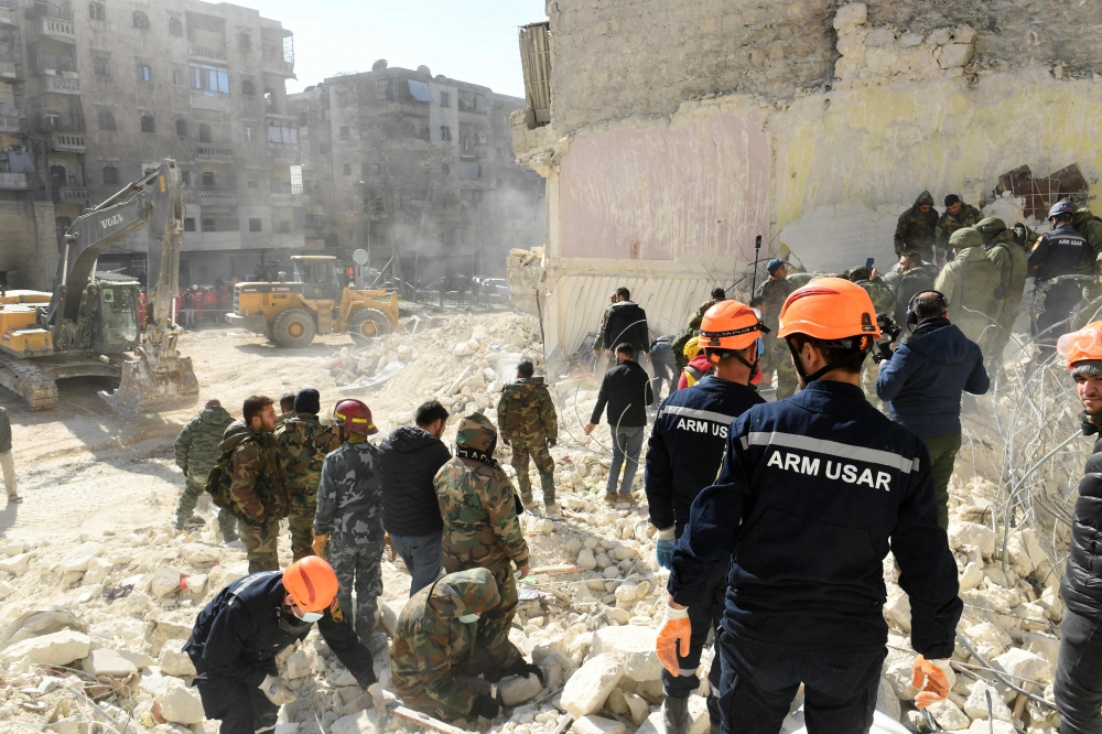 Armenian rescuers (orange helmet) and Syrian soldiers sift through the rubble of a collapsed building in the northern city of Aleppo, searching for victims and survivors days after a deadly earthquake hit Turkey and Syria, on February 9, 2023. (Photo by AFP)