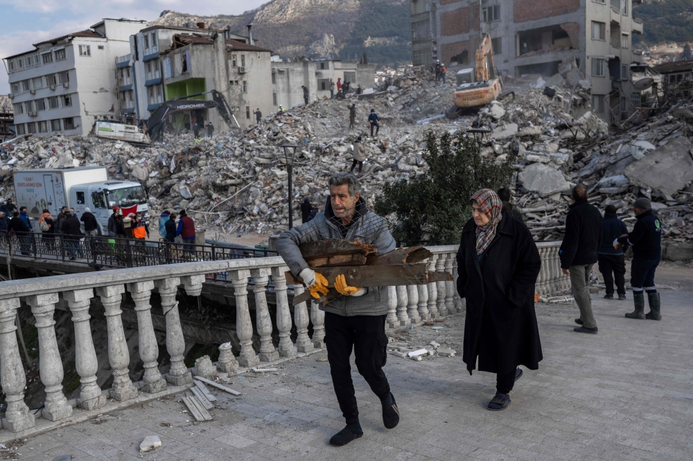 A man holds debris in front of destroyed buildings in the Antakia historical city in Hatay on February 11, 2023, after a 7.8-magnitude earthquake struck the country's south-east. Photo by BULENT KILIC / AFP
