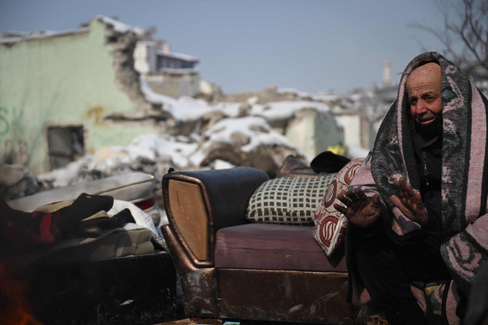 A man sits in front of his collapsed building as rescue teams carry out search operations at Elbistan district of Kahramanmaras on February 11, 2023, after a 7.8-magnitude earthquake struck the country's southeast earlier in the week. (Photo by OZAN KOSE / AFP)