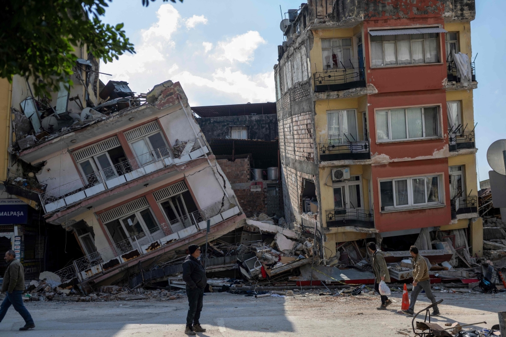 People walk next to damaged buildings in the Antakia historical city in Hatay on February 11, 2023, after a 7.8-magnitude earthquake struck the country's south-east. Photo by BULENT KILIC / AFP