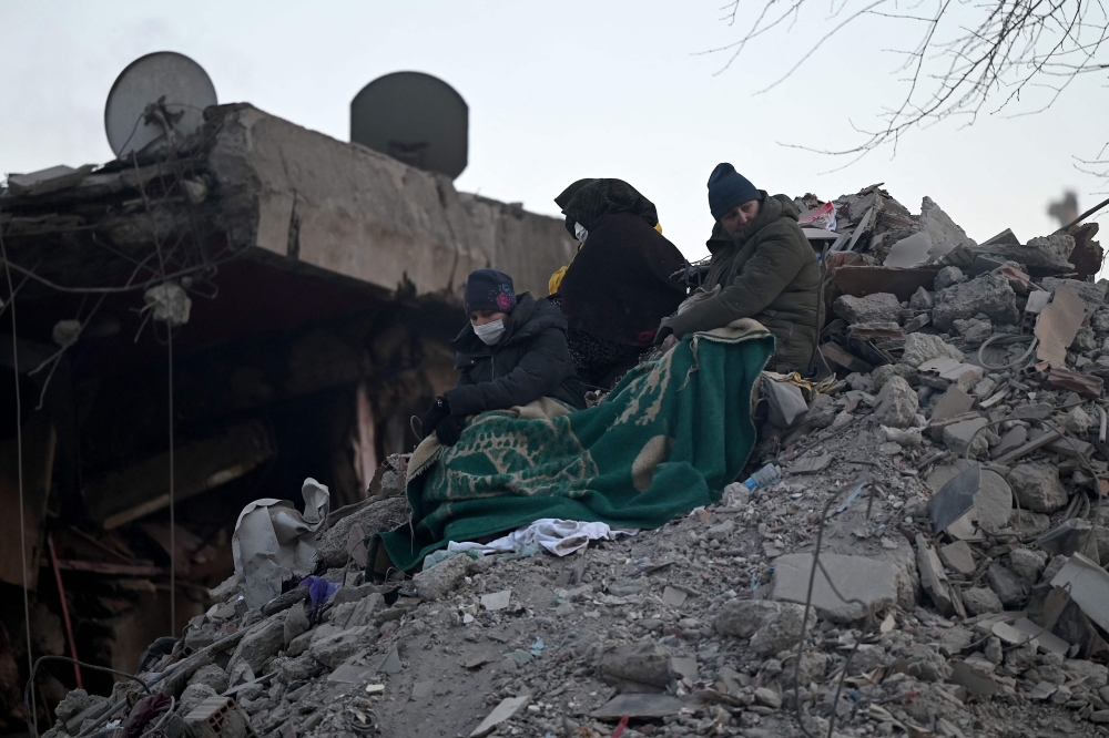 Relatives sit on top of rubble of collapsed buildings, as rescue teams continue to search victims and survivors, in Kahramanmaras on February 12, 2023. (Photo by Ozan Kose / AFP)