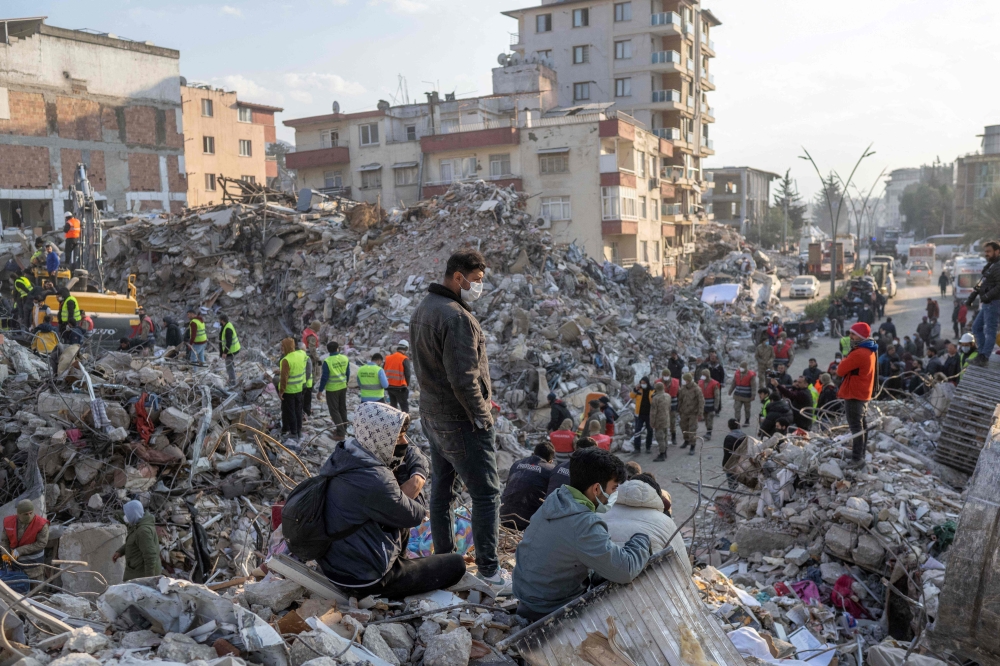People stand on top of rubble of collapsed buildings during rescue operations in Hatay on February 12, 2023, after a 7,8 magnitude earthquake struck the border region of Turkey and Syria earlier in the week. (Photo by BULENT KILIC / AFP)