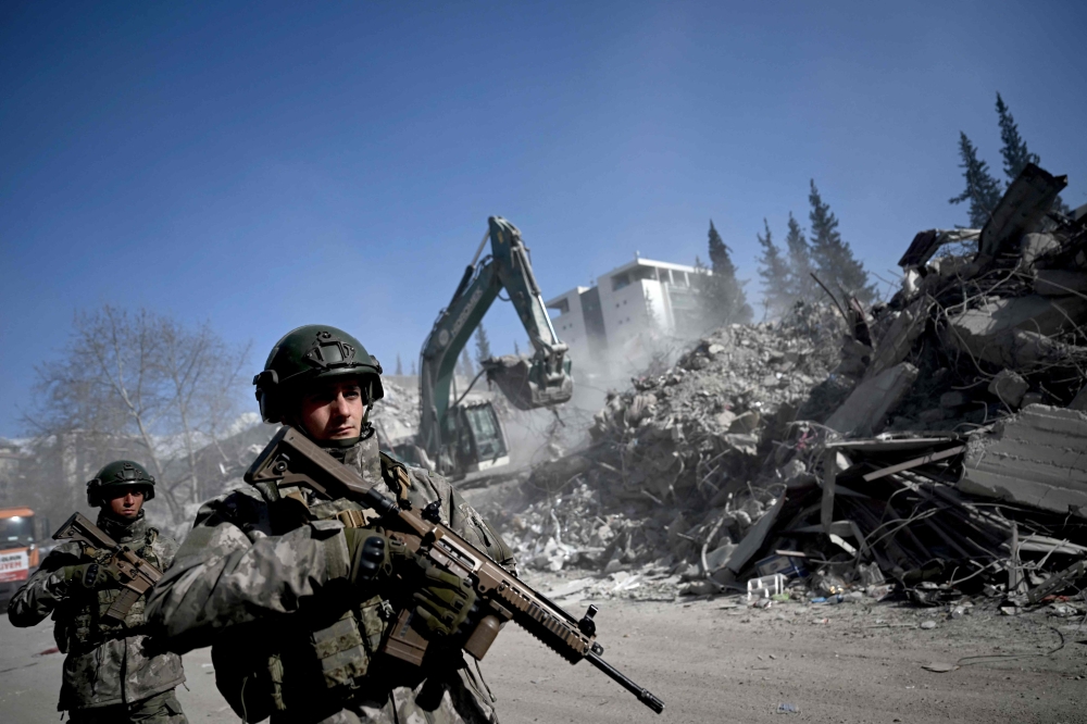 Turkish soldiers patrol next to collapsed buildings in Kahramanmaras on February 13, 2023, as rescue teams continue to search for victims and survivors, after a 7.8 magnitude earthquake struck the border region of Turkey and Syria. (Photo by OZAN KOSE / AFP)