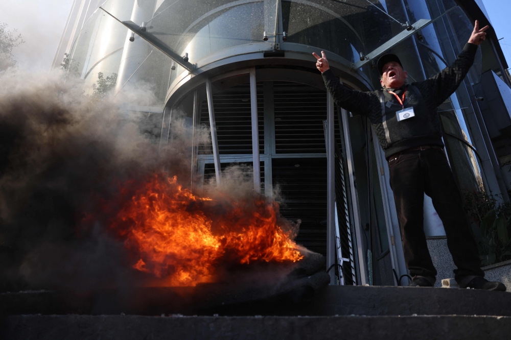 A Lebanese protester flashes the V-sign for victory and shouts slogans as others vandalise banks in Beirut on February 16, 2023 (Photo by Joseph Eid / AFP)