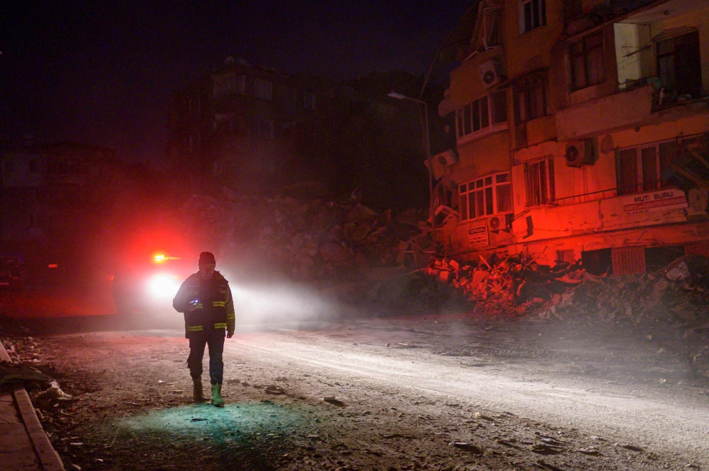 An officer walks in front of a collapsed building in Antakya, south of Hatay on February 16, 2023, ten days after a 7.8-magnitude struck the border region of Turkey and Syria. (Photo by Yasin Akgul / AFP)