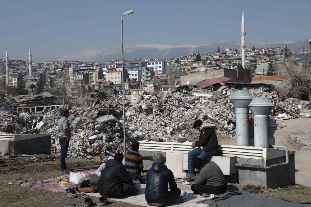 Men look on at the site of collapsed buildings in Kahramanmaras, southeastern Turkey, on February 18, 2023.  (Photo by Zein Al RIFAI / AFP)