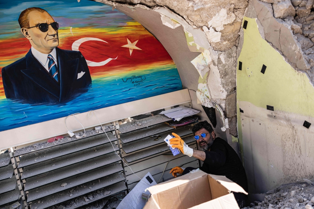 Turkish optician Cuneyt Eroglu, 45-year-old, collects glasses and other stuff from his collapsed shop in Antakya on February 18, 2023. (Photo by Sameer Al-DOUMY / AFP)