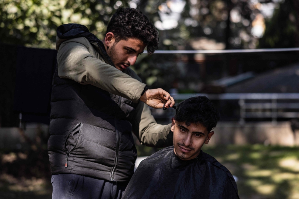 Eighteen-year-old Syrian Mohammed al-Hamo (L) cuts the hair of his 19-year-old brother Sobhi (R) in front of their tent on February 19, 2023. (Photo by Sameer Al-Doumy / AFP)