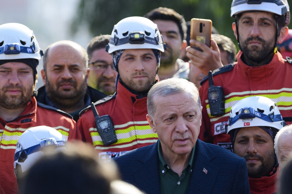 Turkish President Recep Tayyip Erdogan stands with rescue workers as he visits the hard-hit southeastern province of Hatay on February 20, 2023. (Photo by Yasin Akgul / AFP)