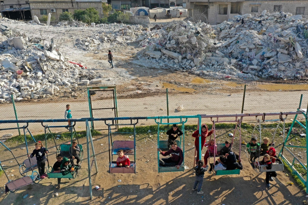 An aerial view shows children playing by the rubble of destroyed buildings in the village of Azmarin in Syria's rebel-held northwestern Idlib province at the border with Turkey on February 18, 2023 following a 7.8-magnitude earthquake. (Photo by OMAR HAJ KADOUR / AFP)