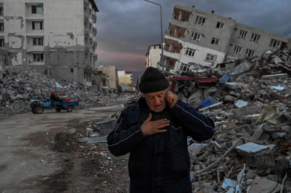 A man speaks on the phone in front of collapsed buildings, a day after a 6.4-magnitude earthquake struck the region, in the coastal city of Samandag, in Turkiye, on February 21, 2023. (Photo by BULENT KILIC / AFP)
