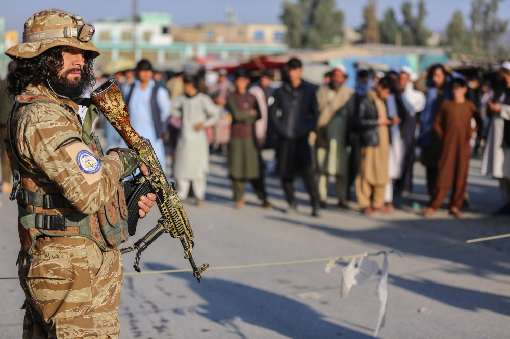 A Taliban security personnel stand guard as Afghan people wait to cross into Pakistan, near the closed Torkham gate at the Torkham border crossing between Afghanistan and Pakistan, in Nangarhar province on February 23, 2023. (Photo by Shafiullah KAKAR / AFP)