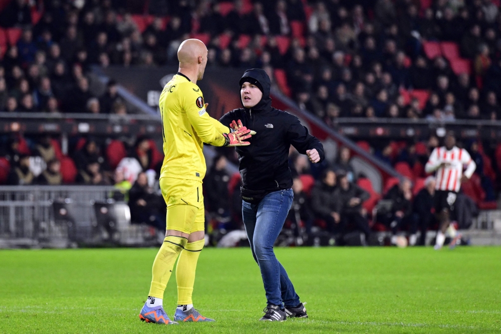 A pitch invader (R) attempts an assault on Sevilla FC goalkeeper Marko Dmitrovic (L) during the UEFA Europa league play-off match between PSV Eindhoven and Sevilla FC at the Phillips stadium in Eindhoven on February 23, 2023. (Photo by Olaf Kraak / ANP / AFP)