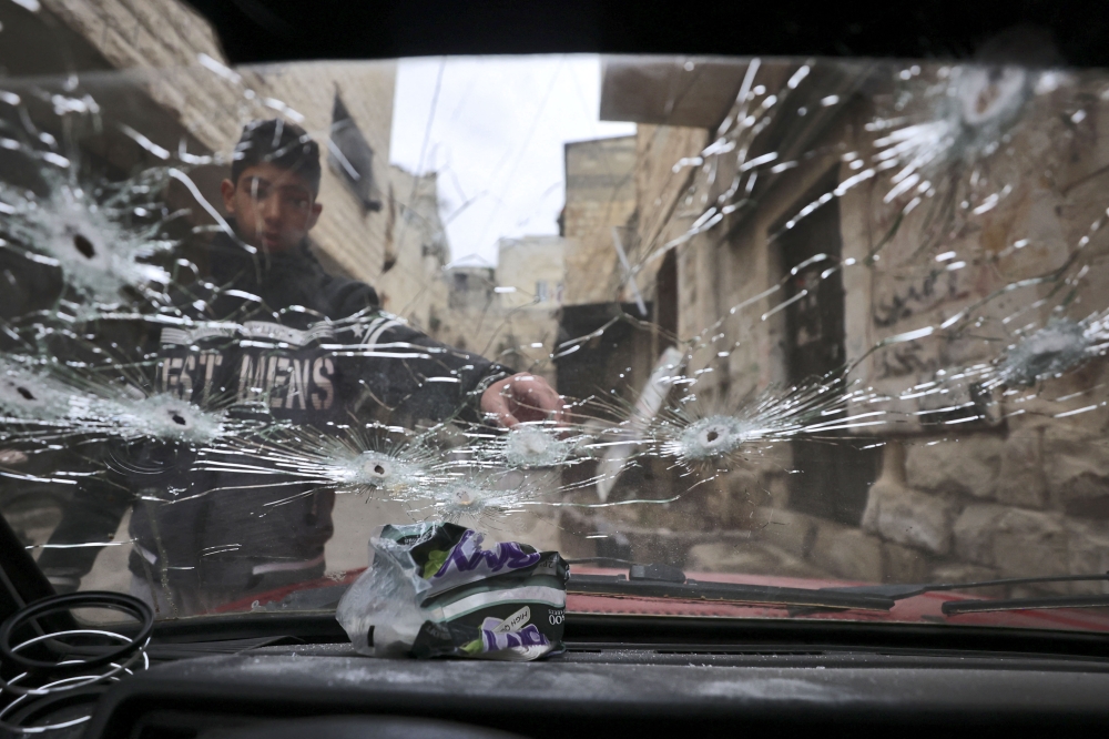 A Palestinian youth points at a bullet-riddled windshield outside a house that was targeted during an Israeli army raid in the Old City of Nablus. (Photo by Zain Jaafar / AFP)
 