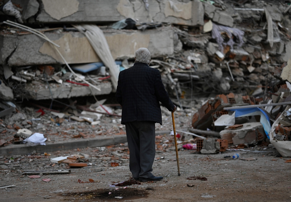A man walks among debris of collapsed buildings in Kahramanmaras, on March 4, 2023, one month after a massive earthquake struck south-east Turkey. Photo by Eylul YASAR / AFP