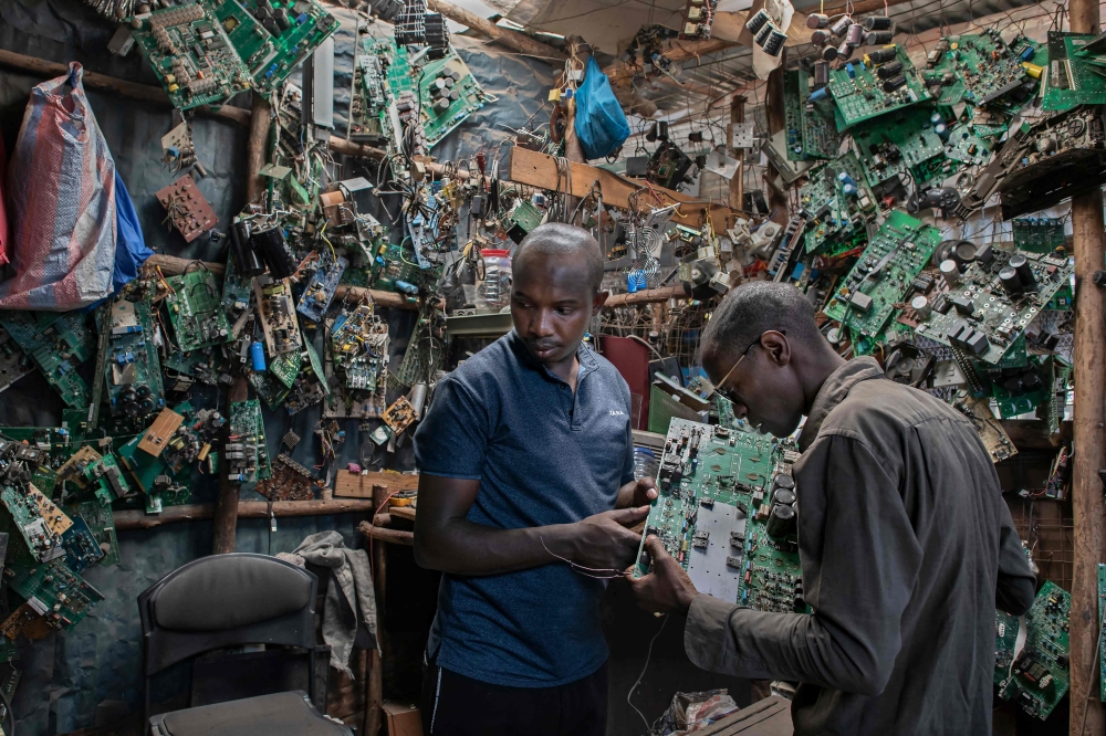 David Gathu (R), 30, and Moses Kiuna (L), 29, both self-taught innovators, rumage through salvaged electrical components at an open-air market stall that specialises in trade in electrical waste in Nairobi on January 31, 2023.  Photos by Tony KARUMBA / AFP