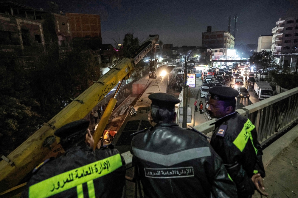 Policemen watch from atop a bridge as a crane is deployed to lift a derailed train at the scene of a railroad accident in the city of Qalyub in Qalyub province, in Egypt's Nile delta region north of the capital on March 7, 2023. (Photo by Khaled DESOUKI / AFP)