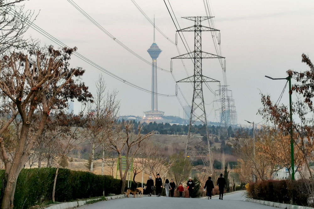 People walk at the Pardisan park with a view of the Milad tower in Tehran, on March 12, 2023. (Photo by Atta Kenare / AFP)