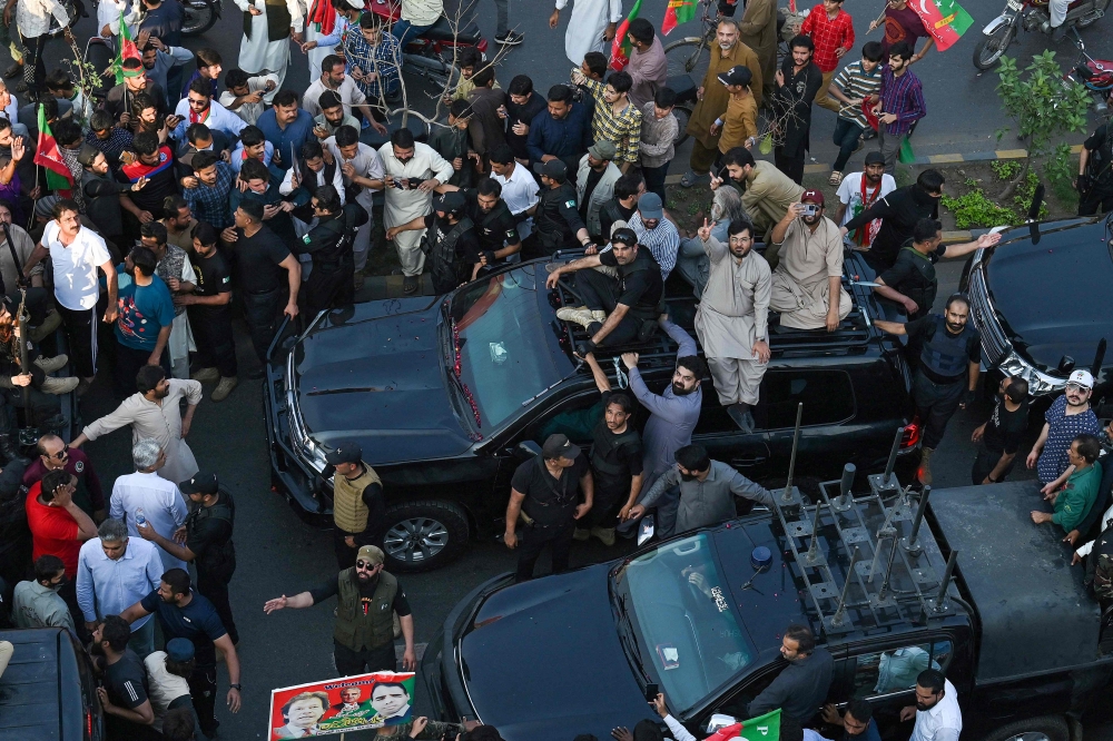 Security personnel and supporters escort a vehicle carrying Pakistan's former prime minister Imran Khan during an election campaign rally for Punjab's provincial assembly to be held next month, in Lahore on March 13, 2023.  (Photo by Arif ALI / AFP)