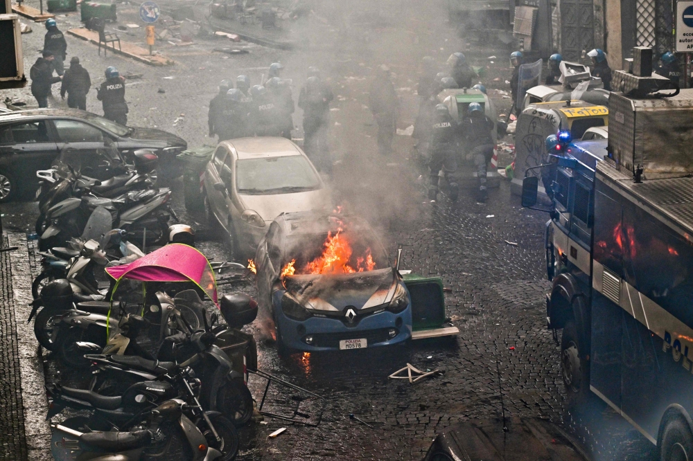 This photo obtained from Italian news agency Ansa shows a police car (Front) burn as Eintracht Frankfurt fans (not in picture) clash with police on March 15, 2023 in downtown Naples prior to the UEFA Champions League round of 16, second leg football match between SSC Napoli and Eintracht Frankfurt to be played at the Diego-Maradona stadium in Naples. Eintracht Frankfurt fans clashed with police on March 15 after arriving in Naples despite not having tickets for their team's Champions League decider with Napoli. (Photo by Ciro FUSCO / ANSA / AFP) 