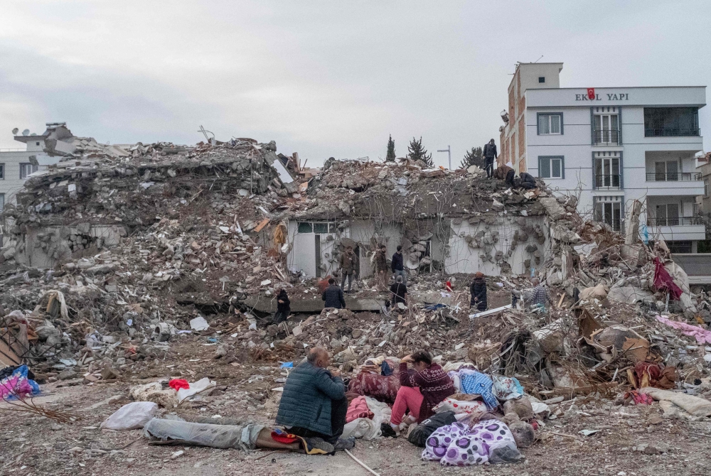 A family sit in front of their former house, destroyed after the 7.8-magnitude earthquake, in Adiyaman, Turkiyes, on March 22, 2023. (Photo by Bulent Kilic / AFP)