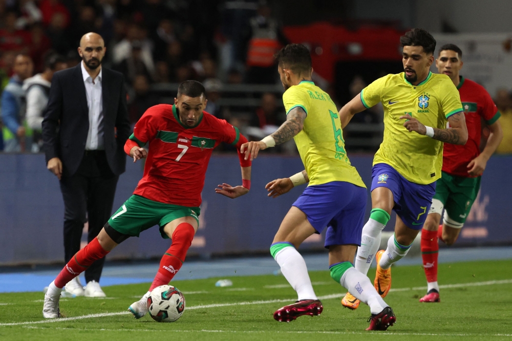 :Morocco's midfielder Hakim Ziyech (L) is marked by Brazil's defender Alex Telles (C) during a friendly football match between Morocco and Brazil at the Ibn Batouta Stadium in Tangier on March 26, 2023. Photo by Fadel Senna / AFP