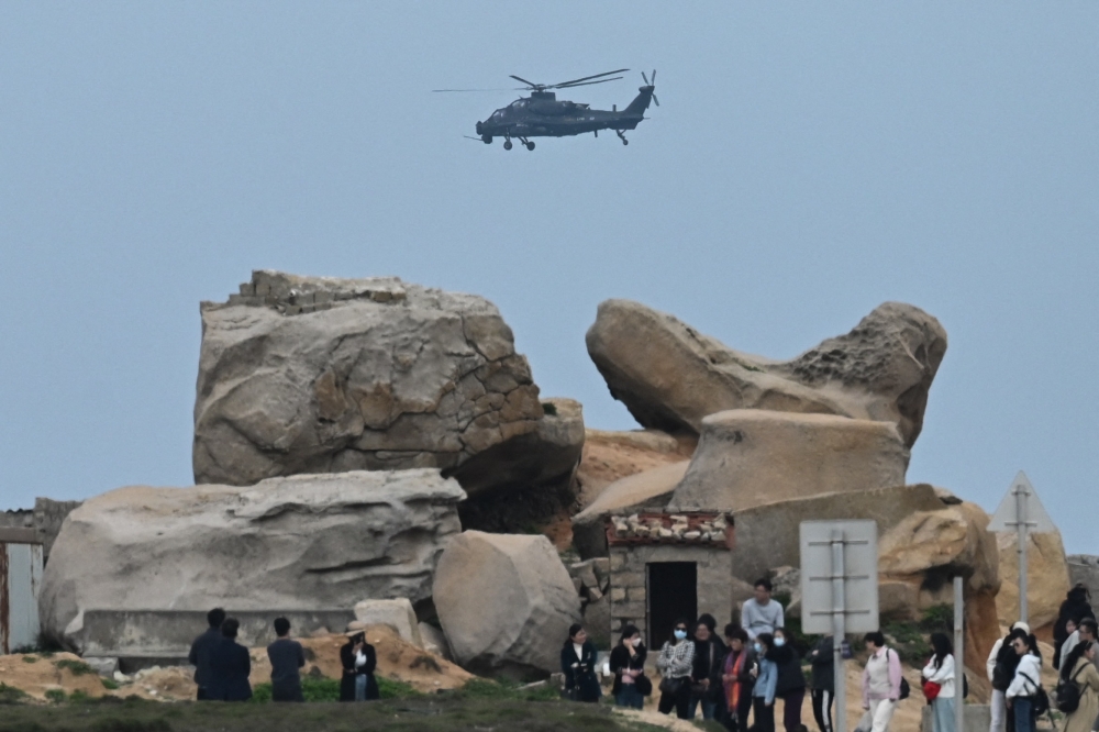 A Chinese military helicopter flies past tourists at a viewing point over the Taiwan Strait, on Pingtan island, the closest point to Taiwan, in China's southeast Fujian province on April 7, 2023. (Photo by GREG BAKER / AFP)