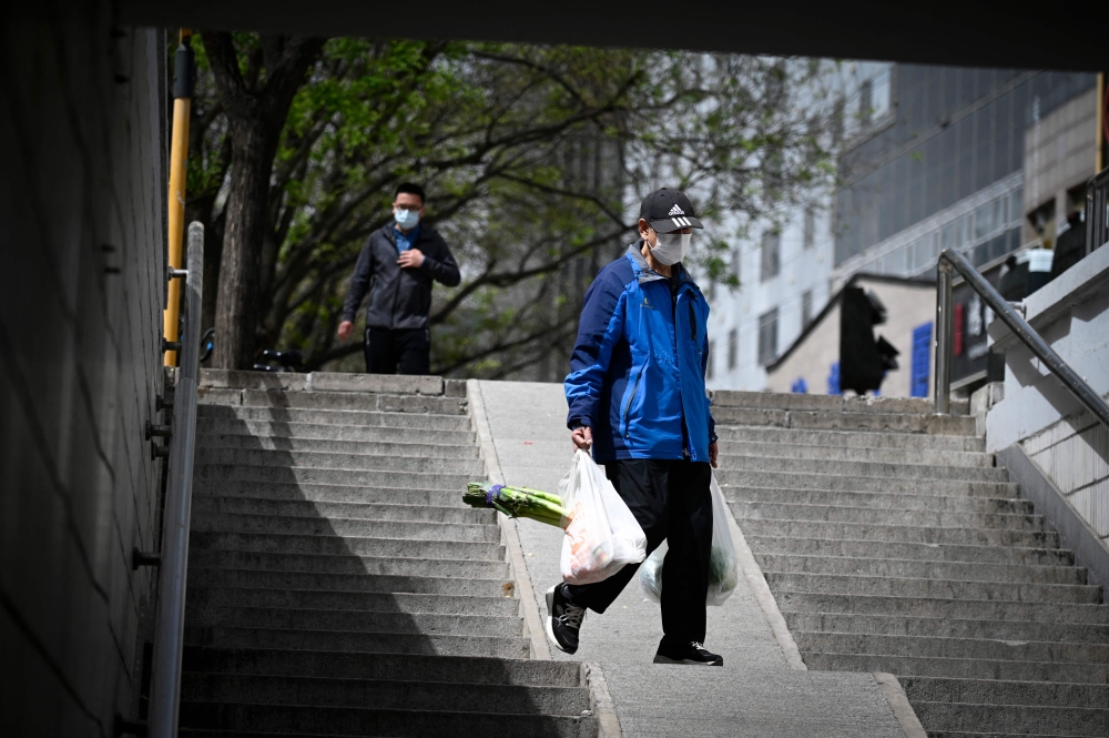 A man carrying bags of vegetables walk through an underpass in Beijing on April 11, 2023. (Photo by WANG Zhao / AFP)